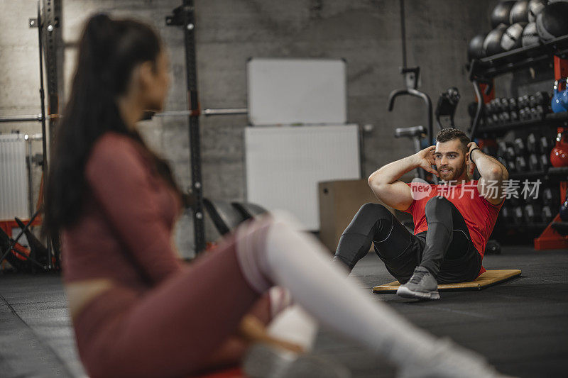 Fit young man doing crunches and fitness girl looking at him in the gym